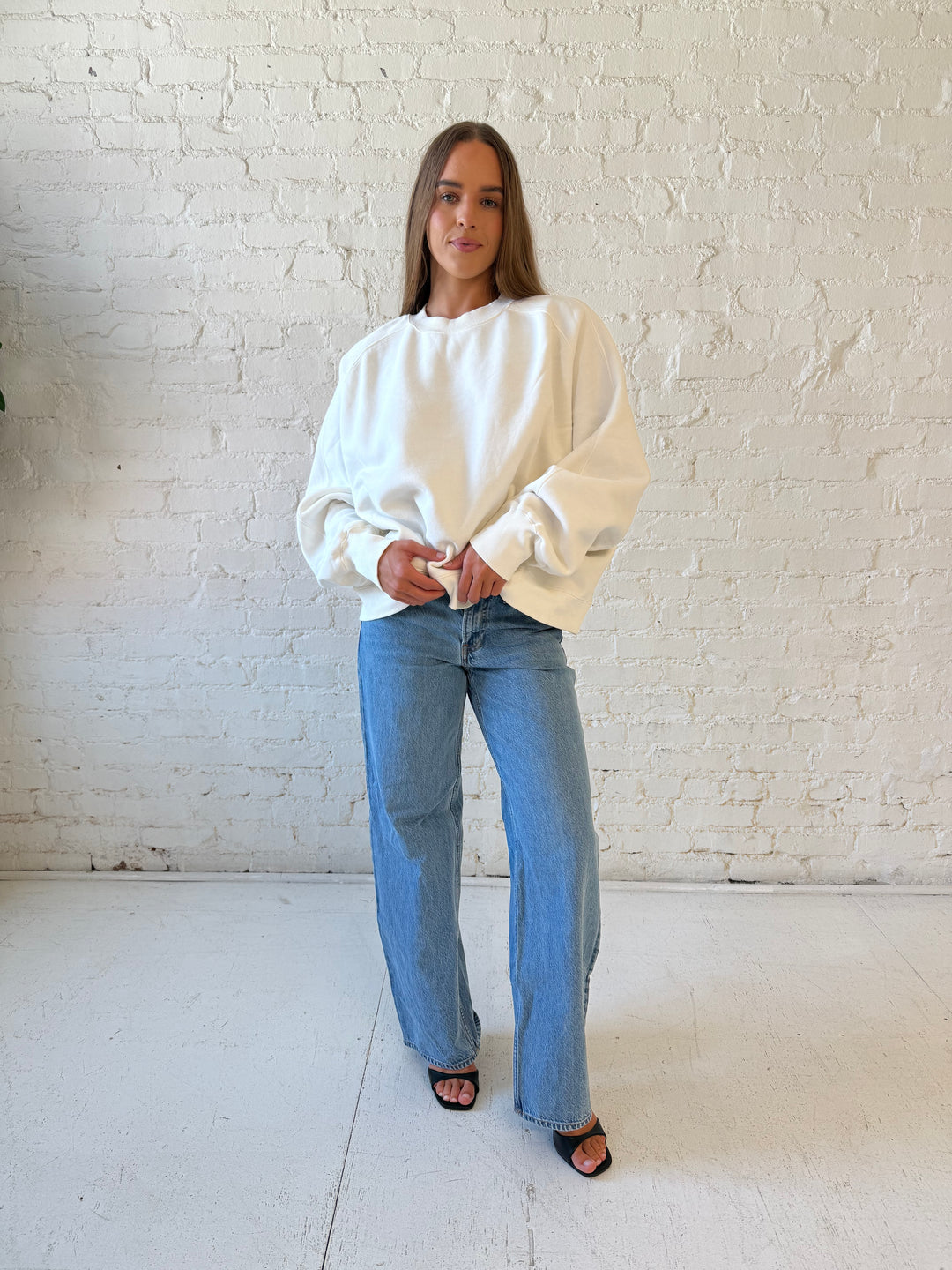 Woman wearing over sized off white crew neck sweatshirt with medium wash jeans. 