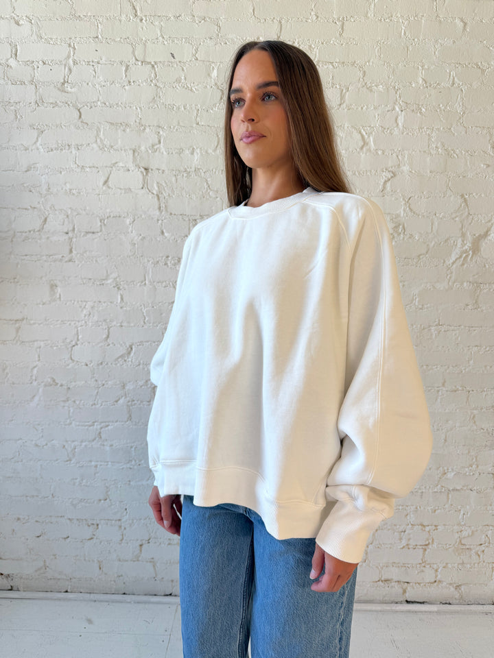 Woman wearing over sized off white crew neck sweatshirt with medium wash jeans. 