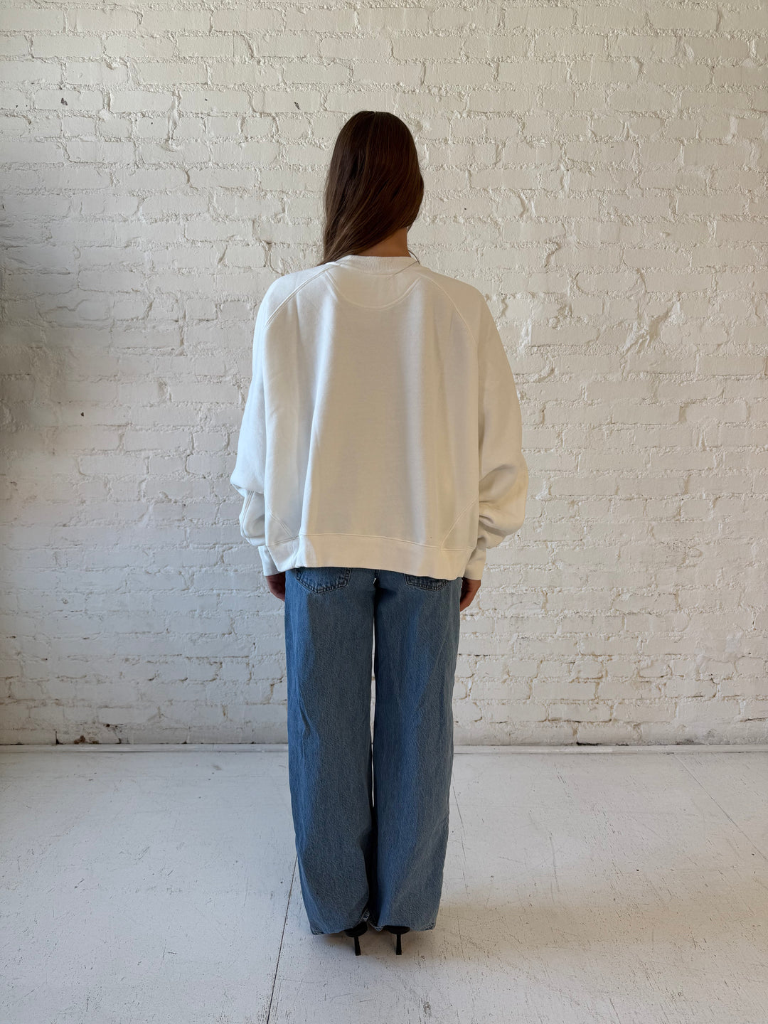 Woman wearing over sized off white crew neck sweatshirt with medium wash jeans. 