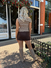 Woman wearing brown plaid asymmetrical top with adjustable side cutout and brown suede mini skirt. 