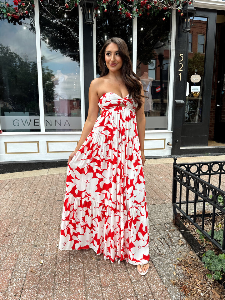 Woman wearing a sleeveless red and white floral mai dress with open back and elastic strap.