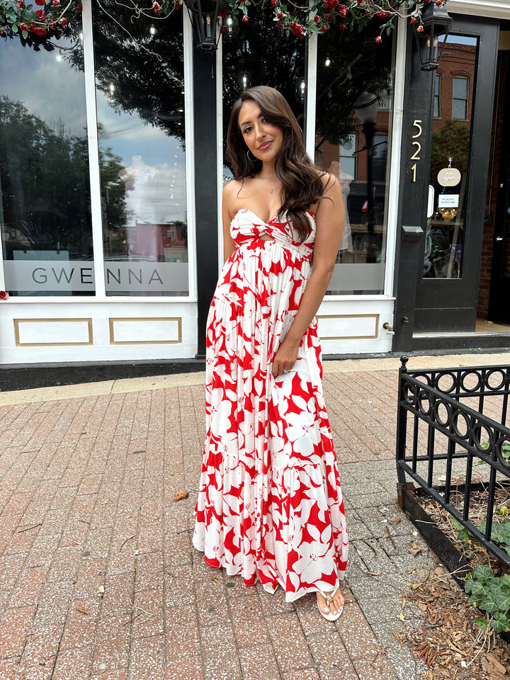 Woman wearing a sleeveless red and white floral mai dress with open back and elastic strap.