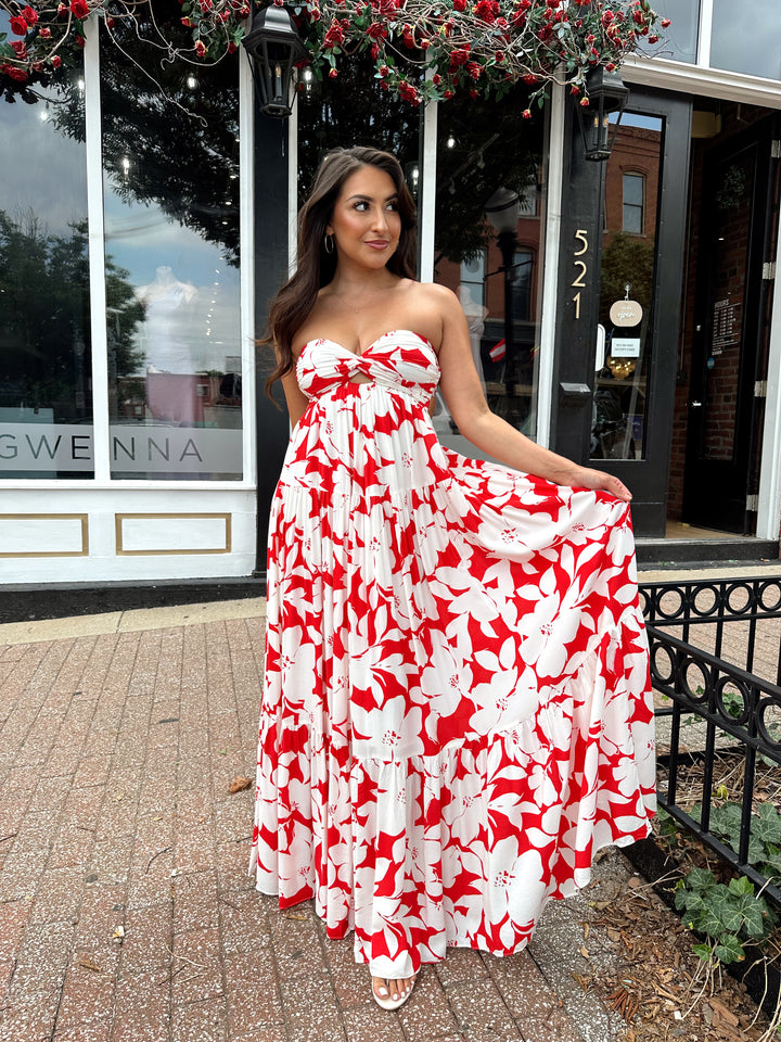 Woman wearing a sleeveless red and white floral mai dress with open back and elastic strap.