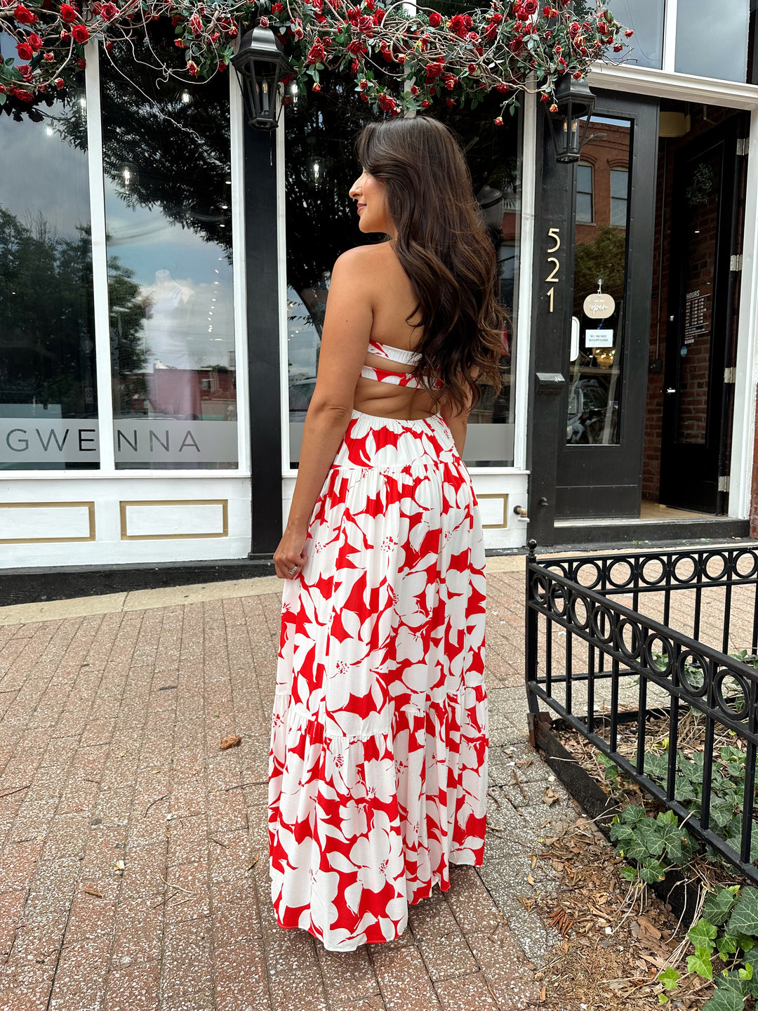Woman wearing a sleeveless red and white floral mai dress with open back and elastic strap.