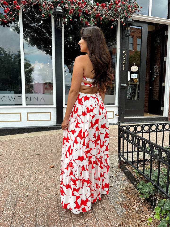 Woman wearing a sleeveless red and white floral mai dress with open back and elastic strap.