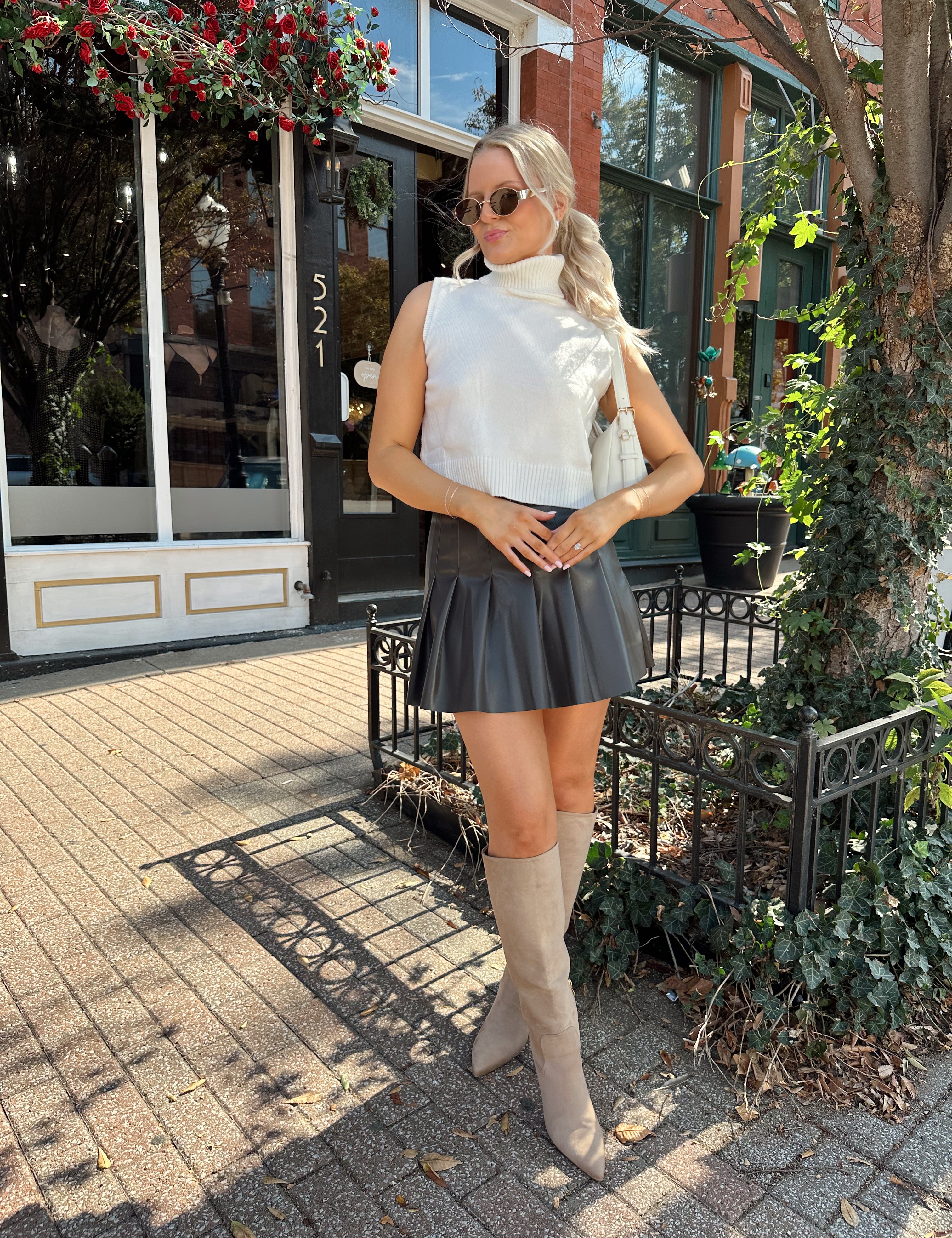 Woman wearing cream sleeveless turtle neck top with brown leather mini skirt.