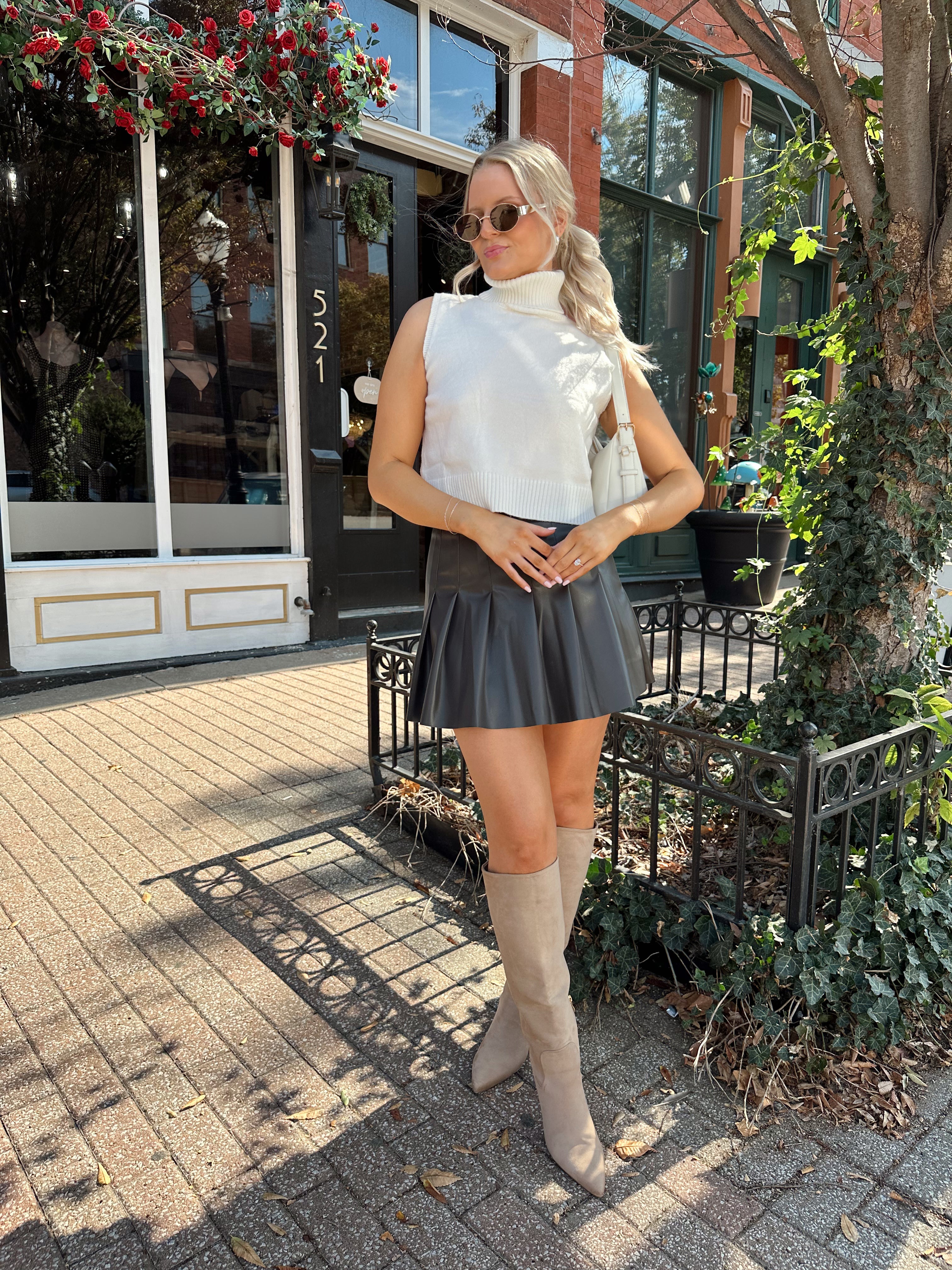 Woman wearing cream sleeveless turtle neck top with brown leather mini skirt.