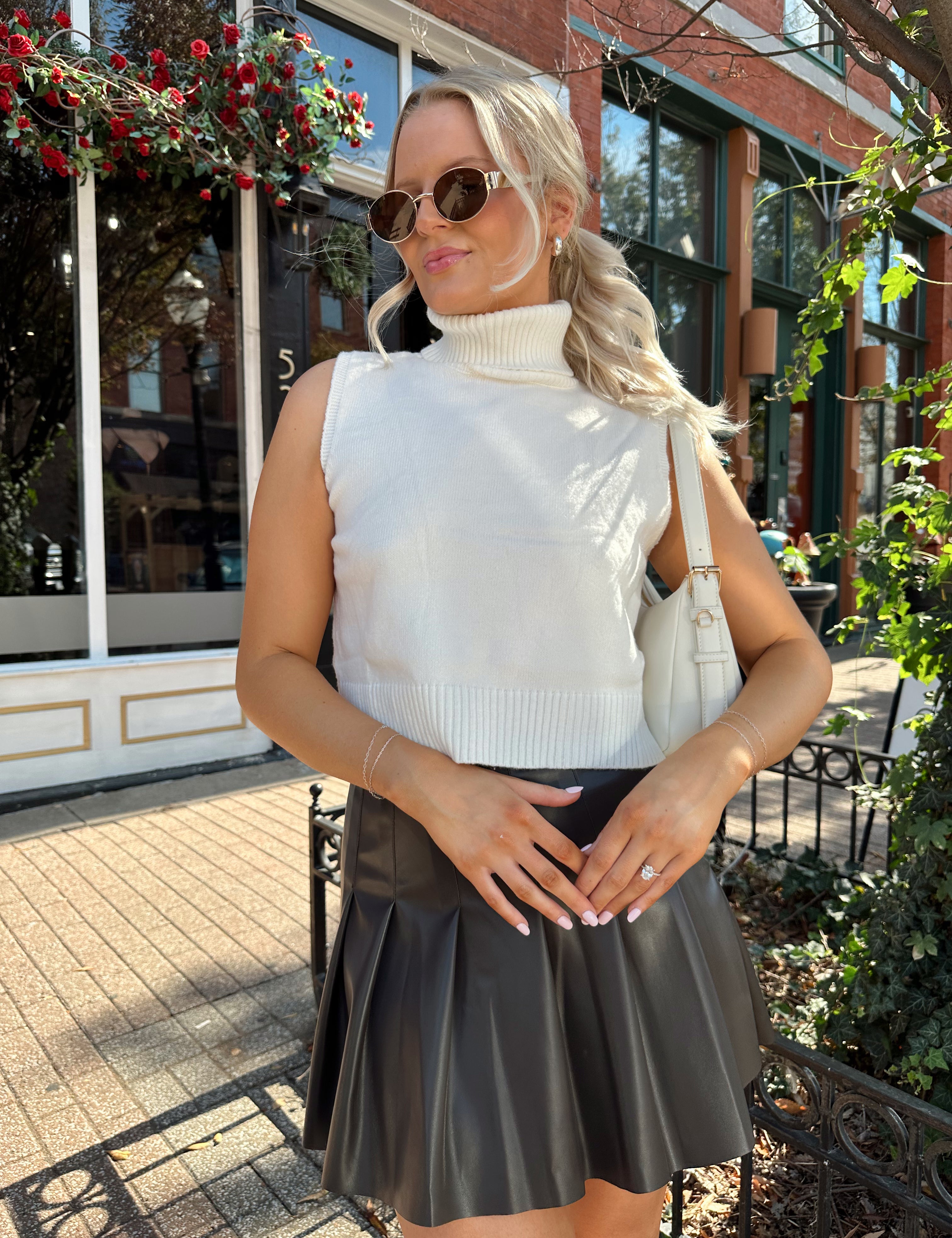 Woman wearing cream sleeveless turtle neck top with brown leather mini skirt.
