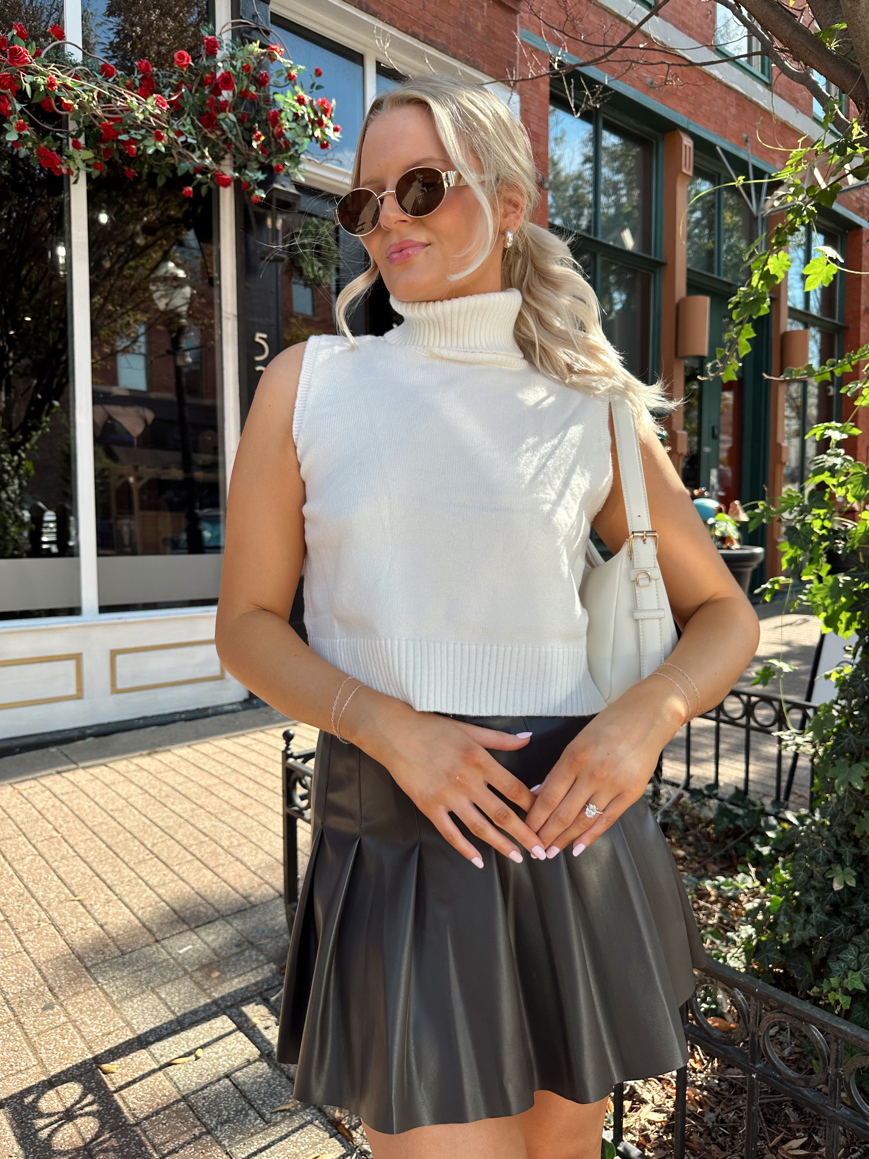 Woman wearing cream sleeveless turtle neck top with brown leather mini skirt.