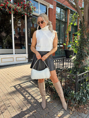 Woman wearing cream sleeveless turtle neck top with brown leather mini skirt.