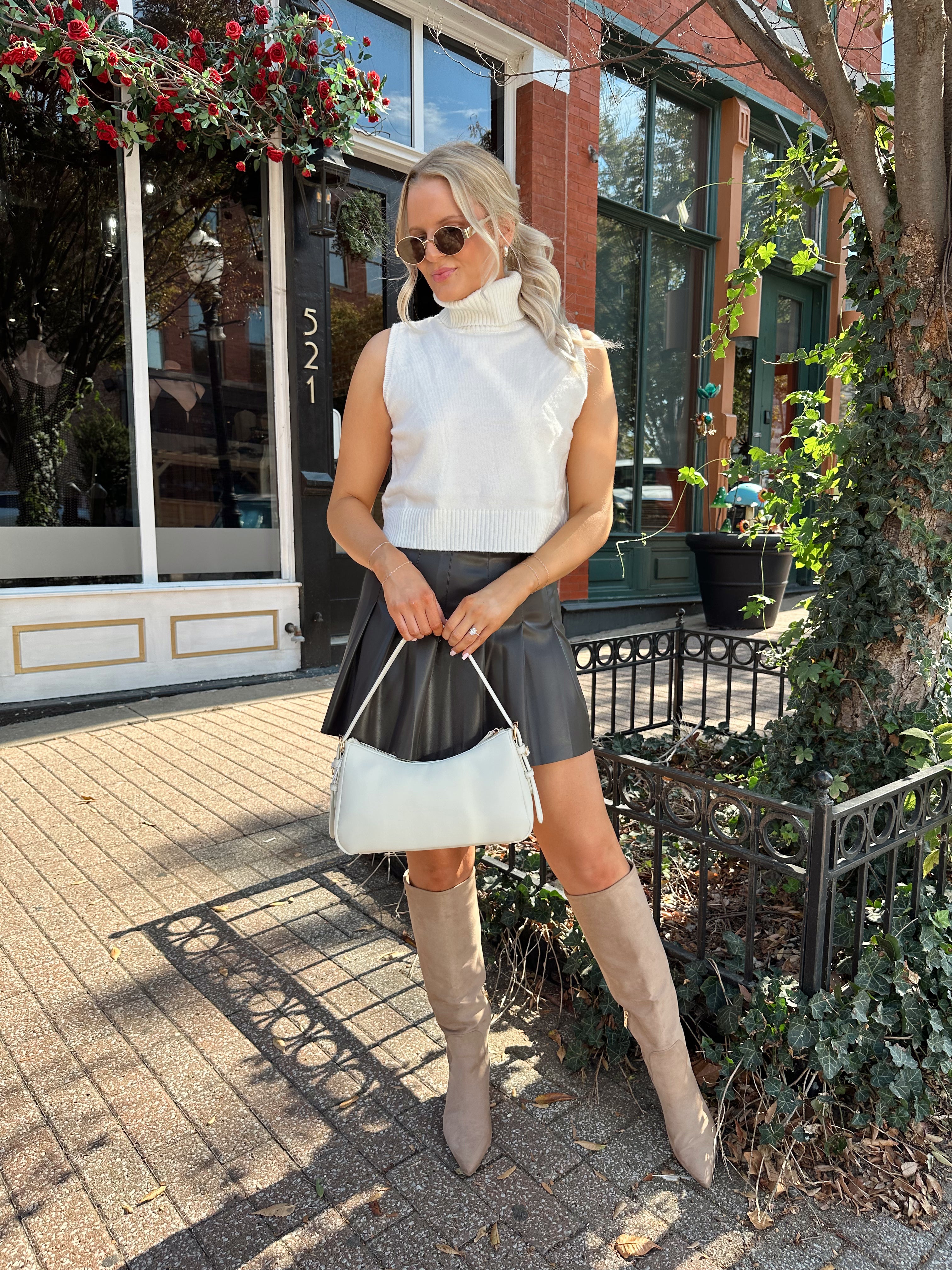 Woman wearing cream sleeveless turtle neck top with brown leather mini skirt.