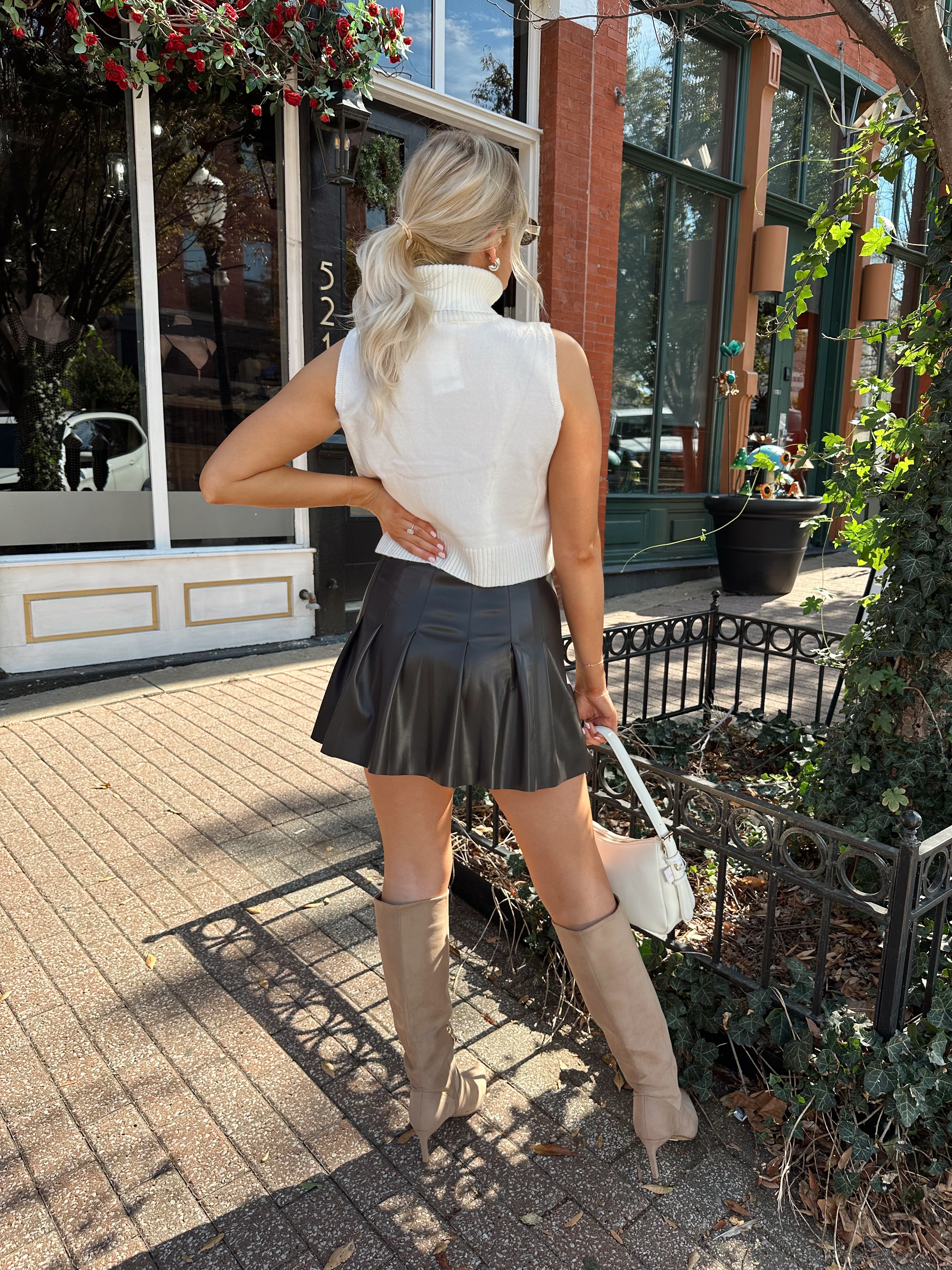 Woman wearing cream sleeveless turtle neck top with brown leather mini skirt.