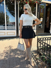 Woman wearing cream knit short sleeve sweater top with black mini skirt. 