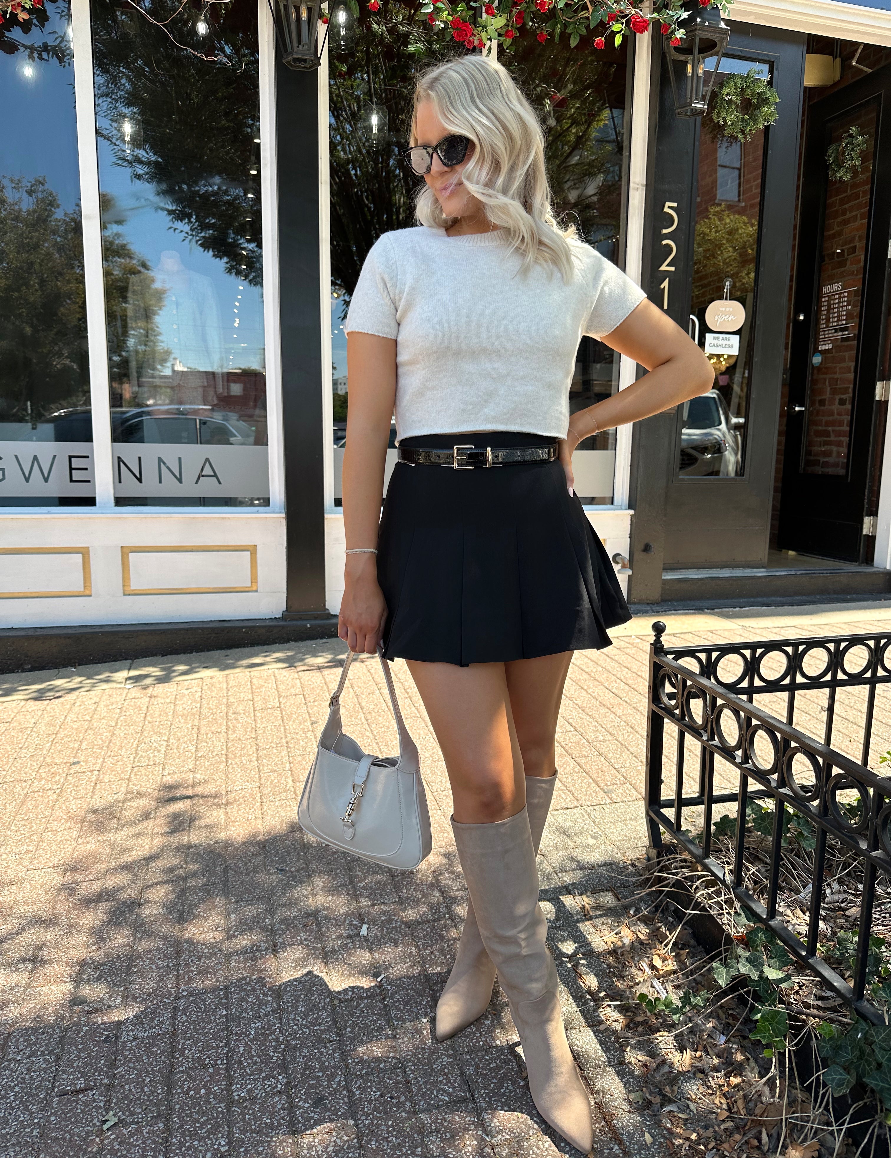 Woman wearing cream knit short sleeve sweater top with black mini skirt. 