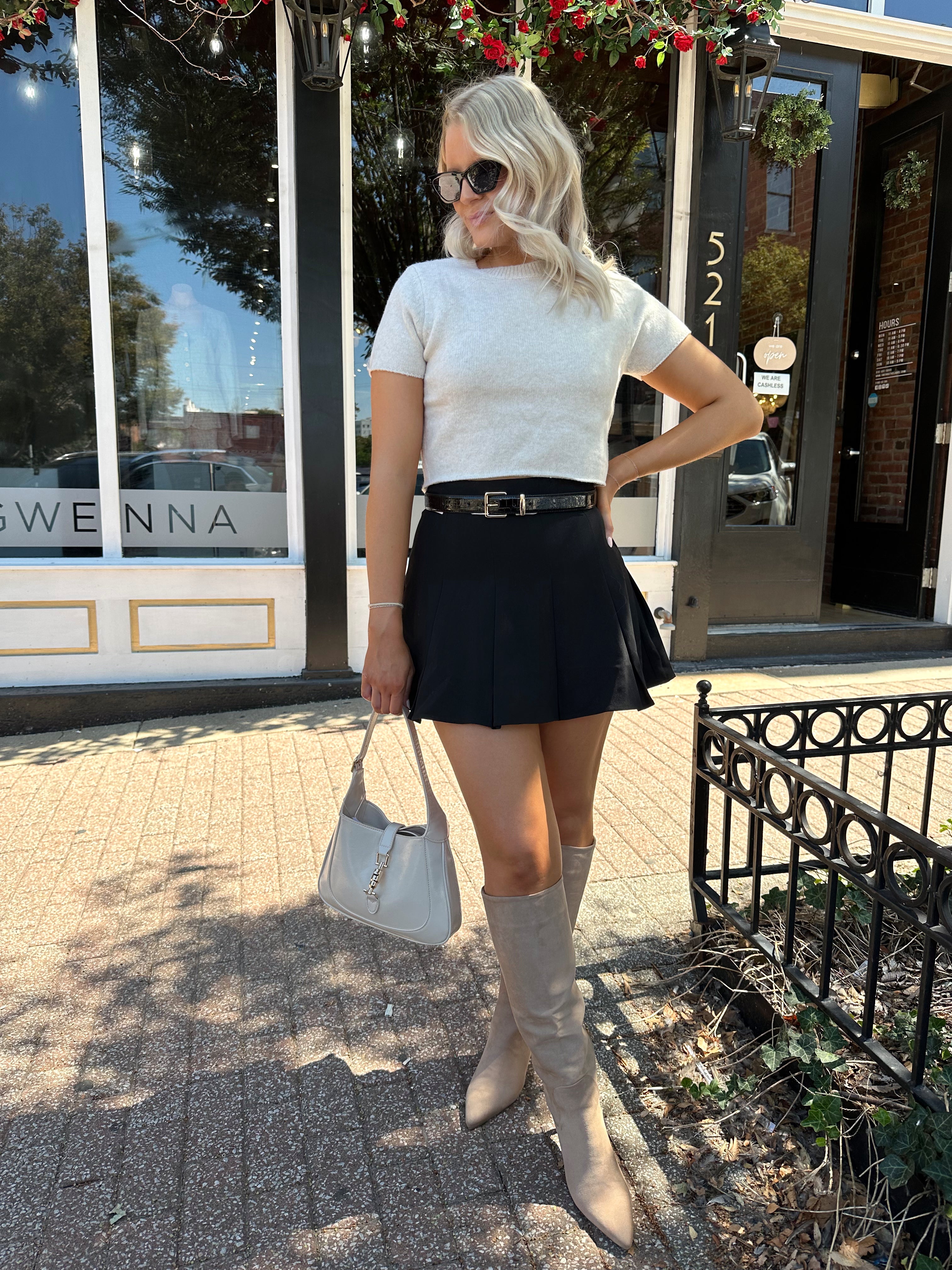 Woman wearing cream knit short sleeve sweater top with black mini skirt. 