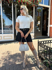 Woman wearing cream knit short sleeve sweater top with black mini skirt. 