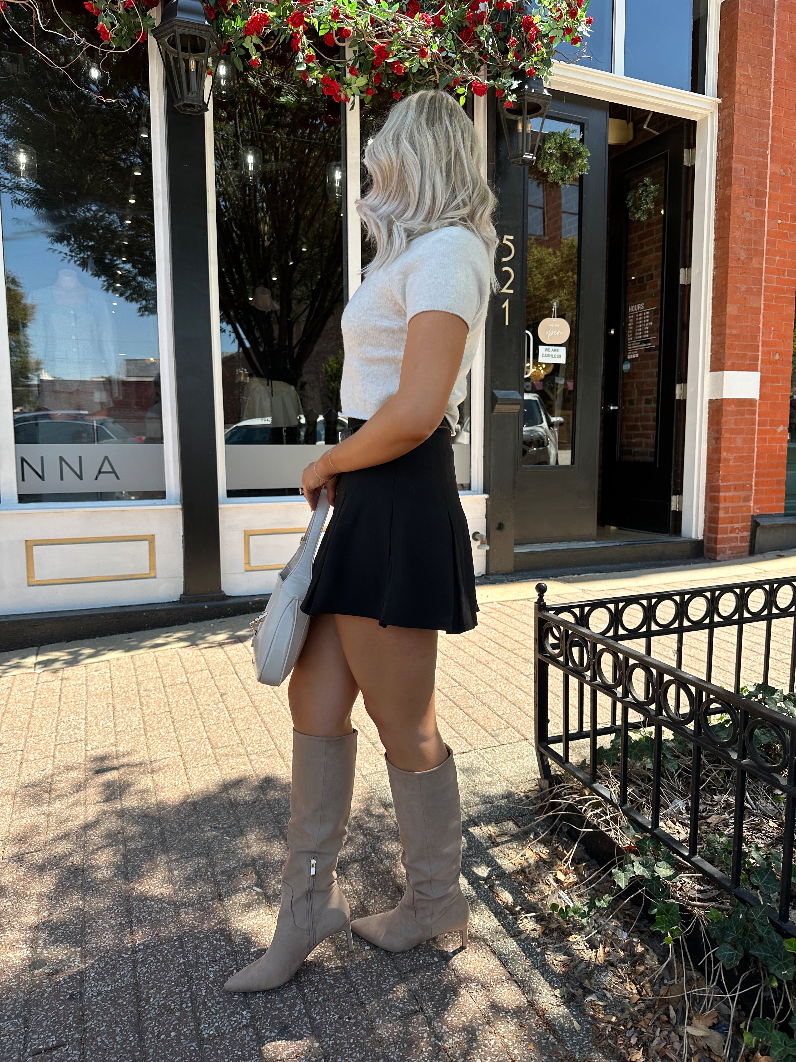 Woman wearing cream knit short sleeve sweater top with black mini skirt. 