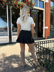 Woman wearing cream knit short sleeve sweater top with black mini skirt. 