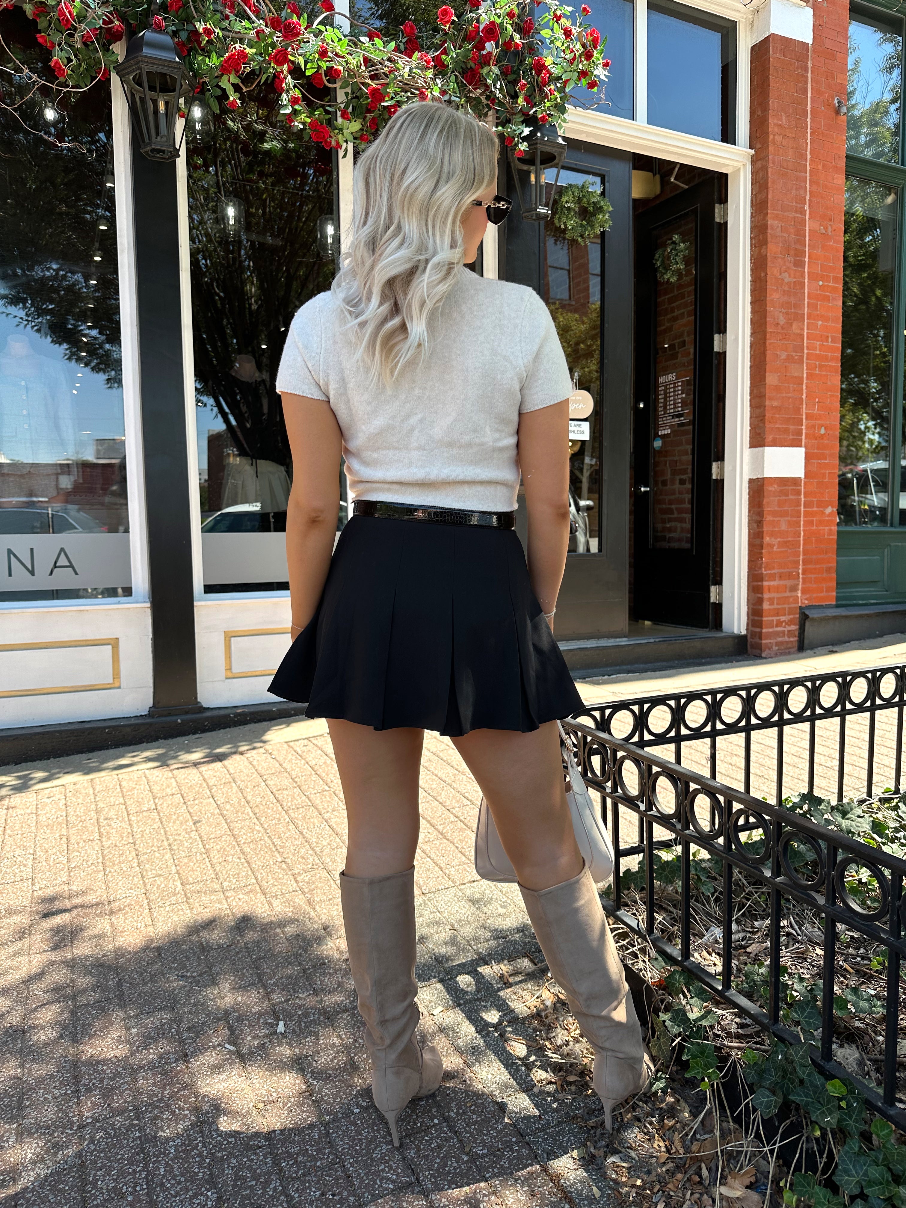 Woman wearing cream knit short sleeve sweater top with black mini skirt. 