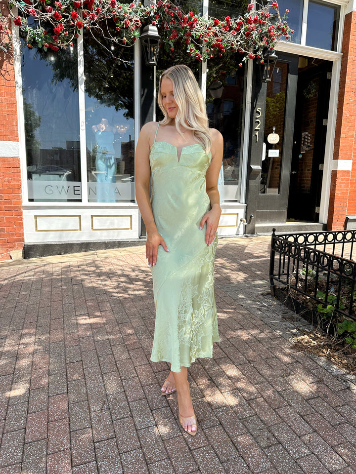 Woman wearing light green jacquard satin maxi dress with adjustable spaghetti straps.