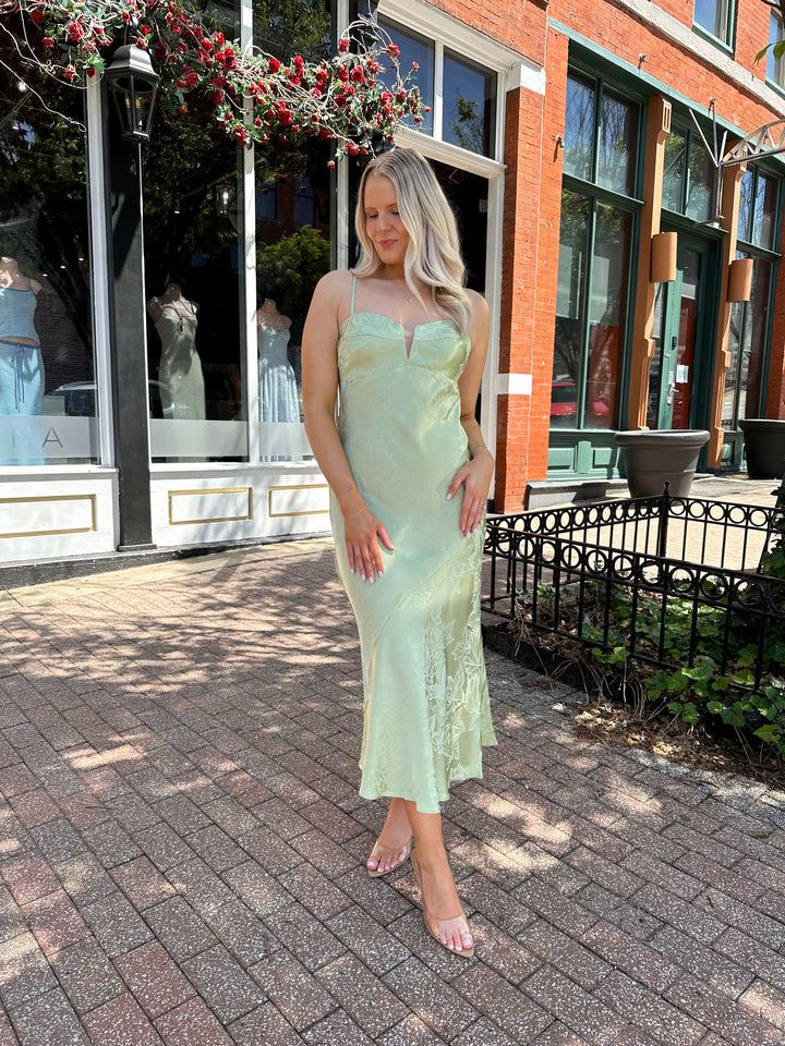 Woman wearing light green jacquard satin maxi dress with adjustable spaghetti straps.