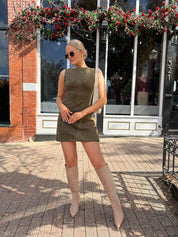 Woman wearing olive green suede mini dress with high neckline and v-back.