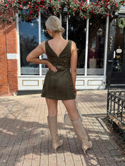 Woman wearing olive green suede mini dress with high neckline and v-back.