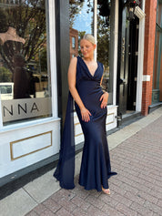 Woman wearing navy blue satin maxi dress with cowl front and back and detachable sash. 