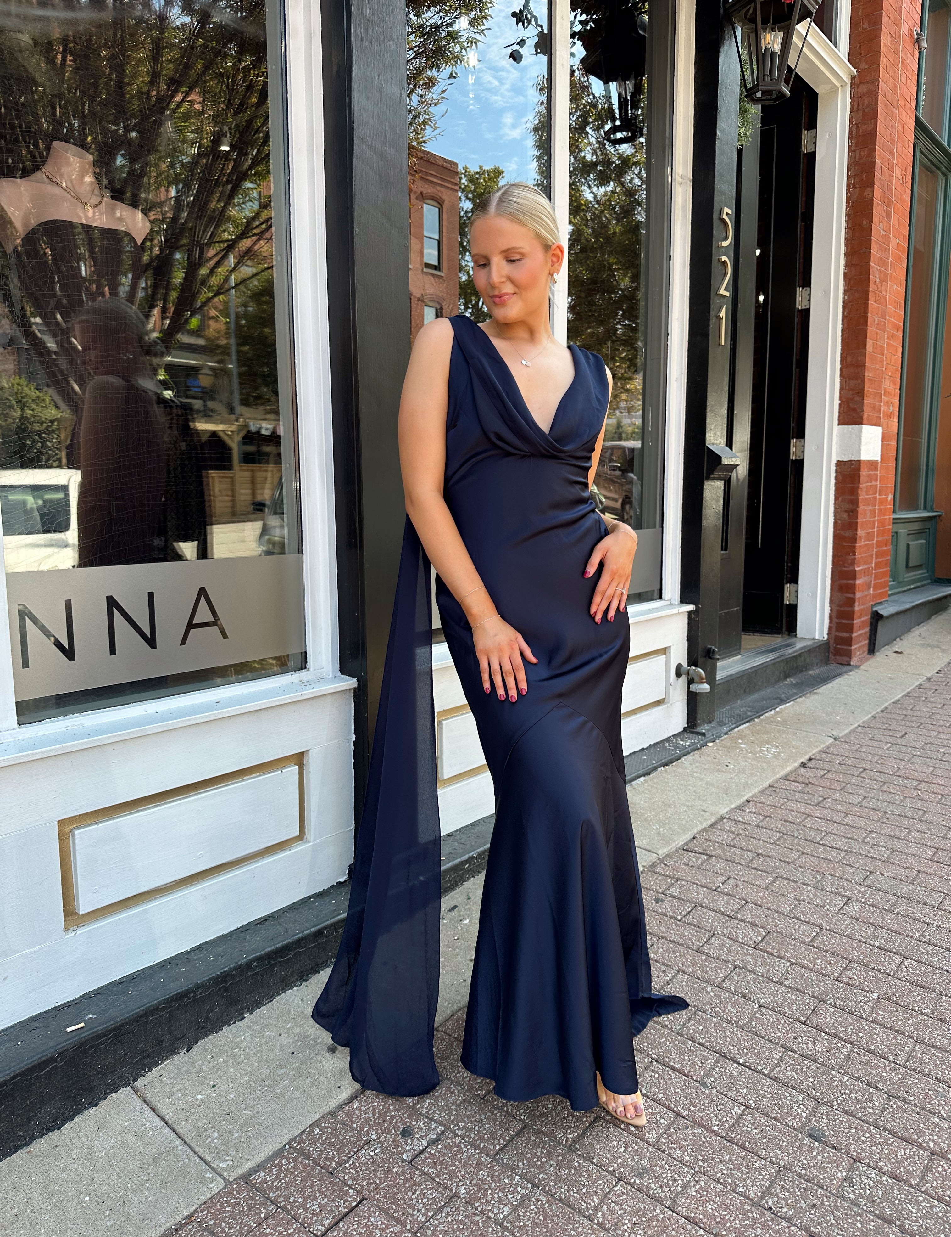 Woman wearing navy blue satin maxi dress with cowl front and back and detachable sash. 