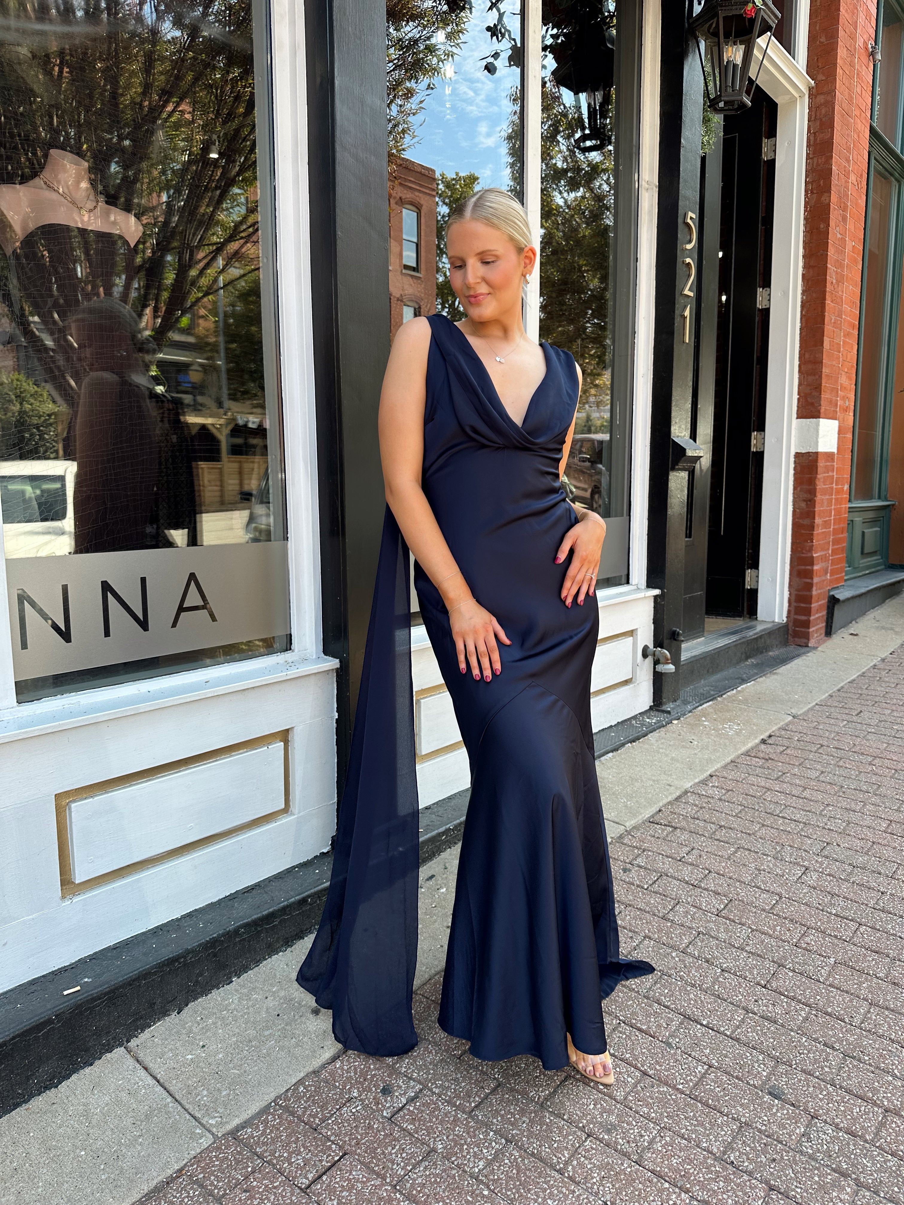 Woman wearing navy blue satin maxi dress with cowl front and back and detachable sash. 