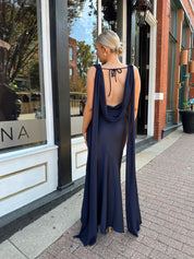 Woman wearing navy blue satin maxi dress with cowl front and back and detachable sash. 