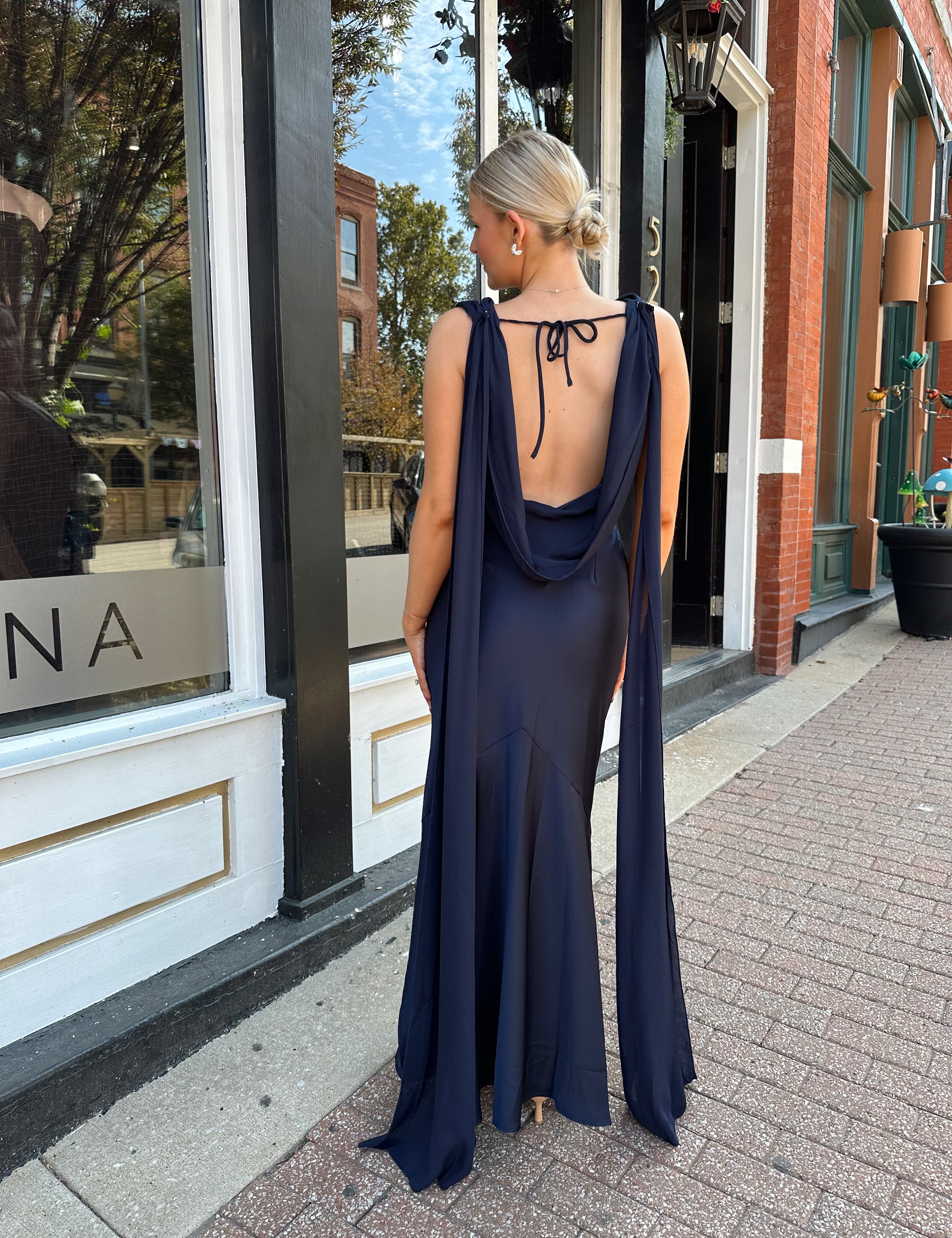 Woman wearing navy blue satin maxi dress with cowl front and back and detachable sash. 