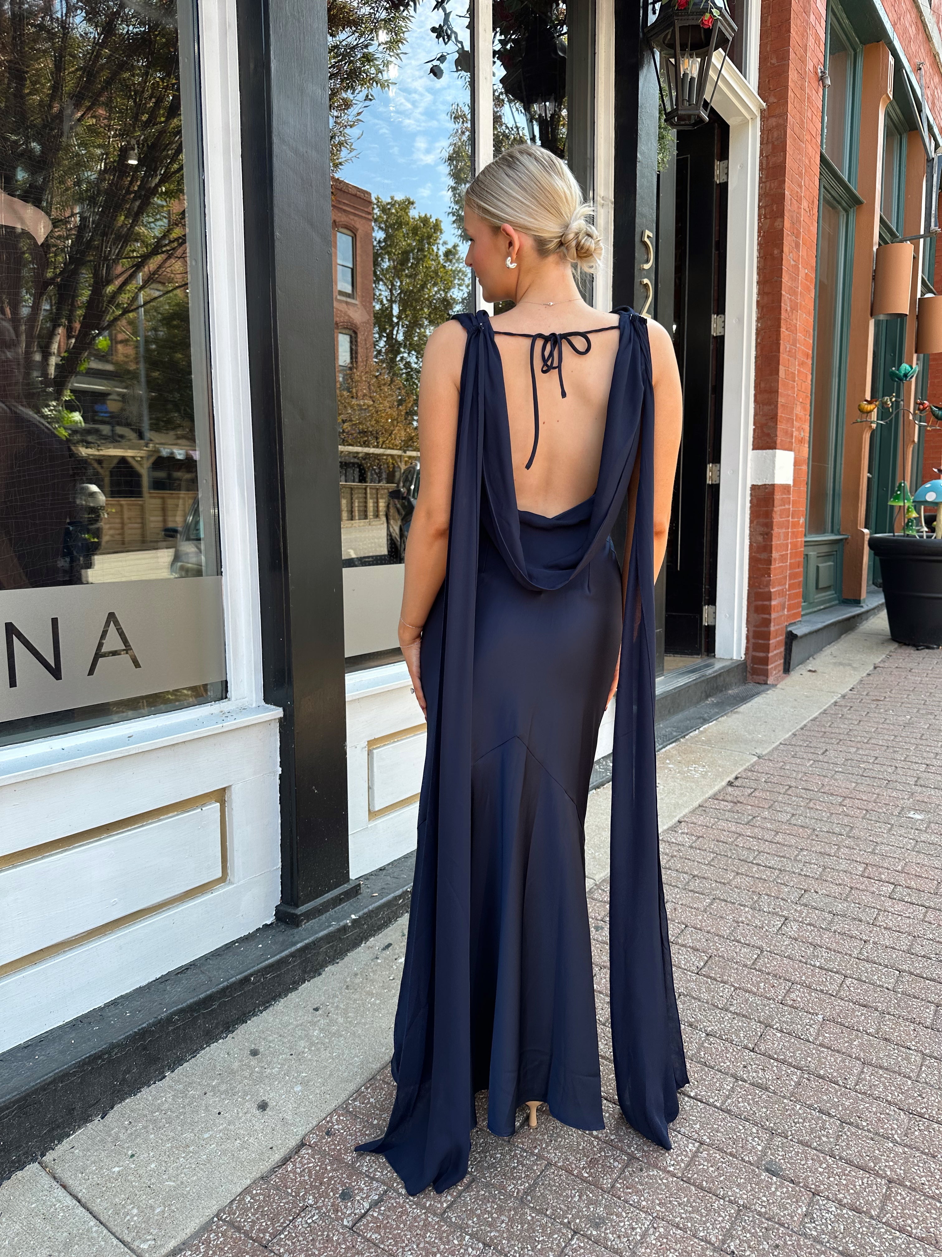 Woman wearing navy blue satin maxi dress with cowl front and back and detachable sash. 