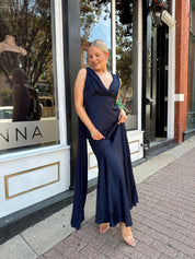 Woman wearing navy blue satin maxi dress with cowl front and back and detachable sash. 
