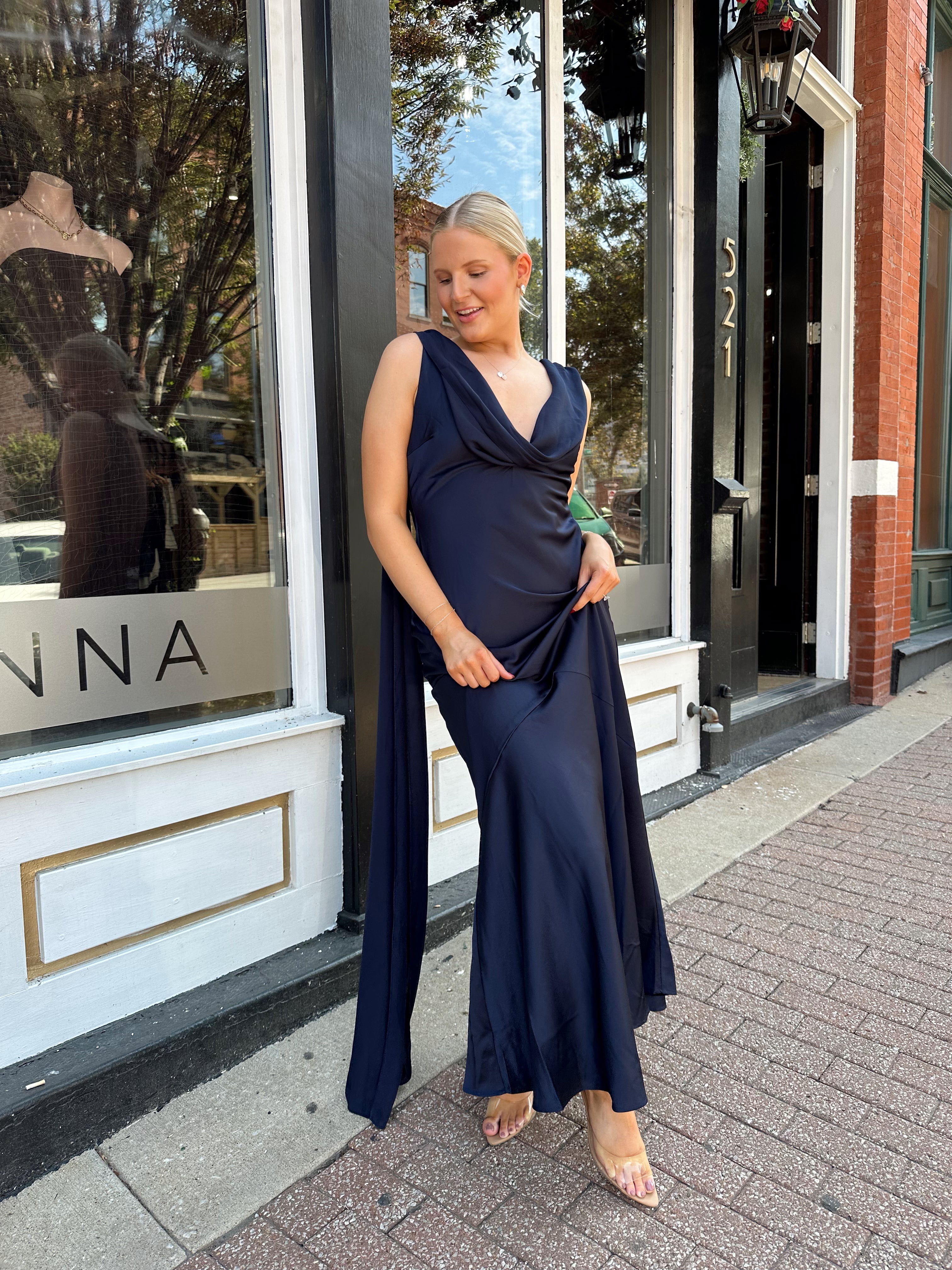 Woman wearing navy blue satin maxi dress with cowl front and back and detachable sash. 