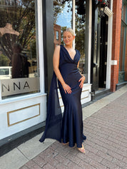 Woman wearing navy blue satin maxi dress with cowl front and back and detachable sash. 