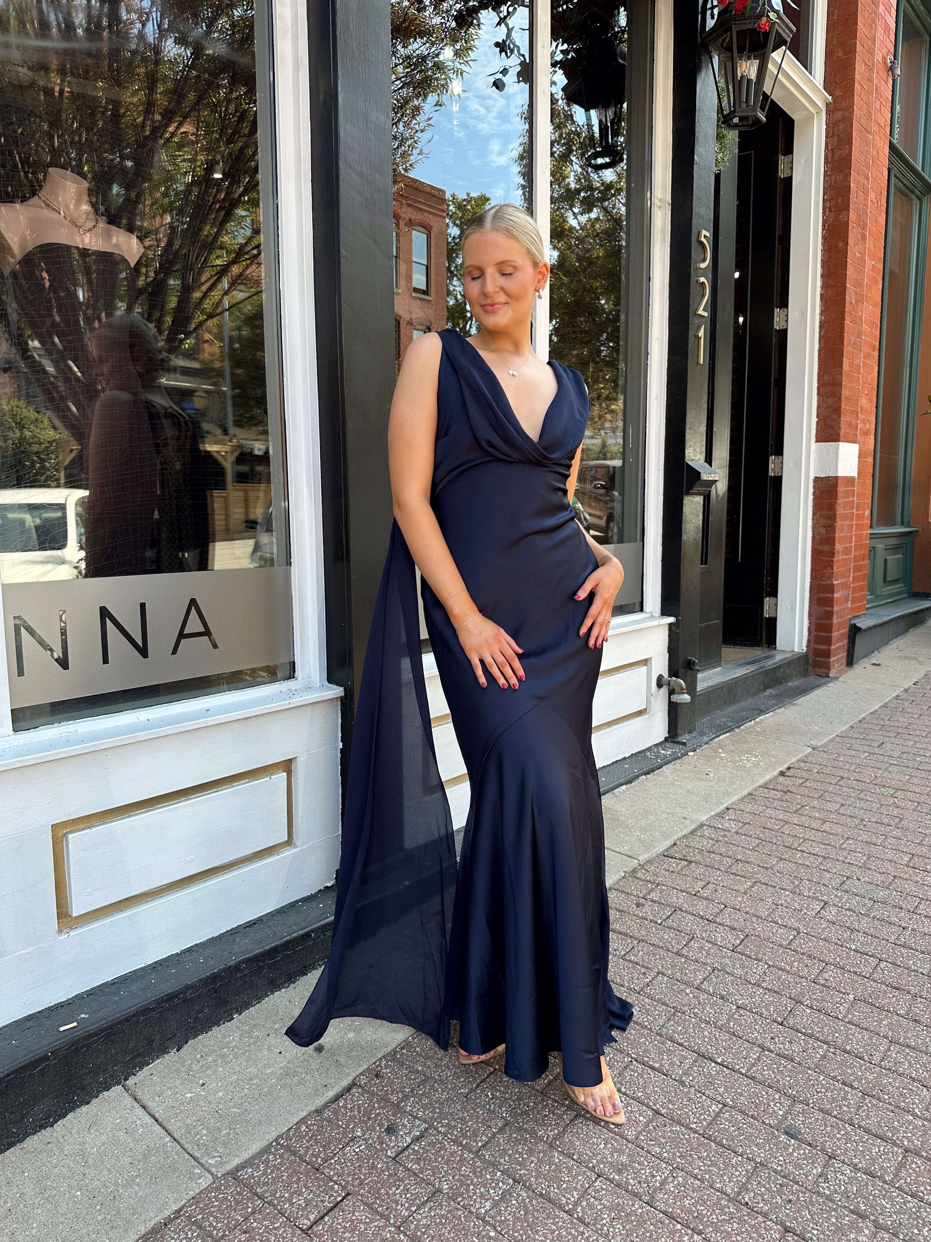 Woman wearing navy blue satin maxi dress with cowl front and back and detachable sash. 