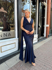Woman wearing navy blue satin maxi dress with cowl front and back and detachable sash. 