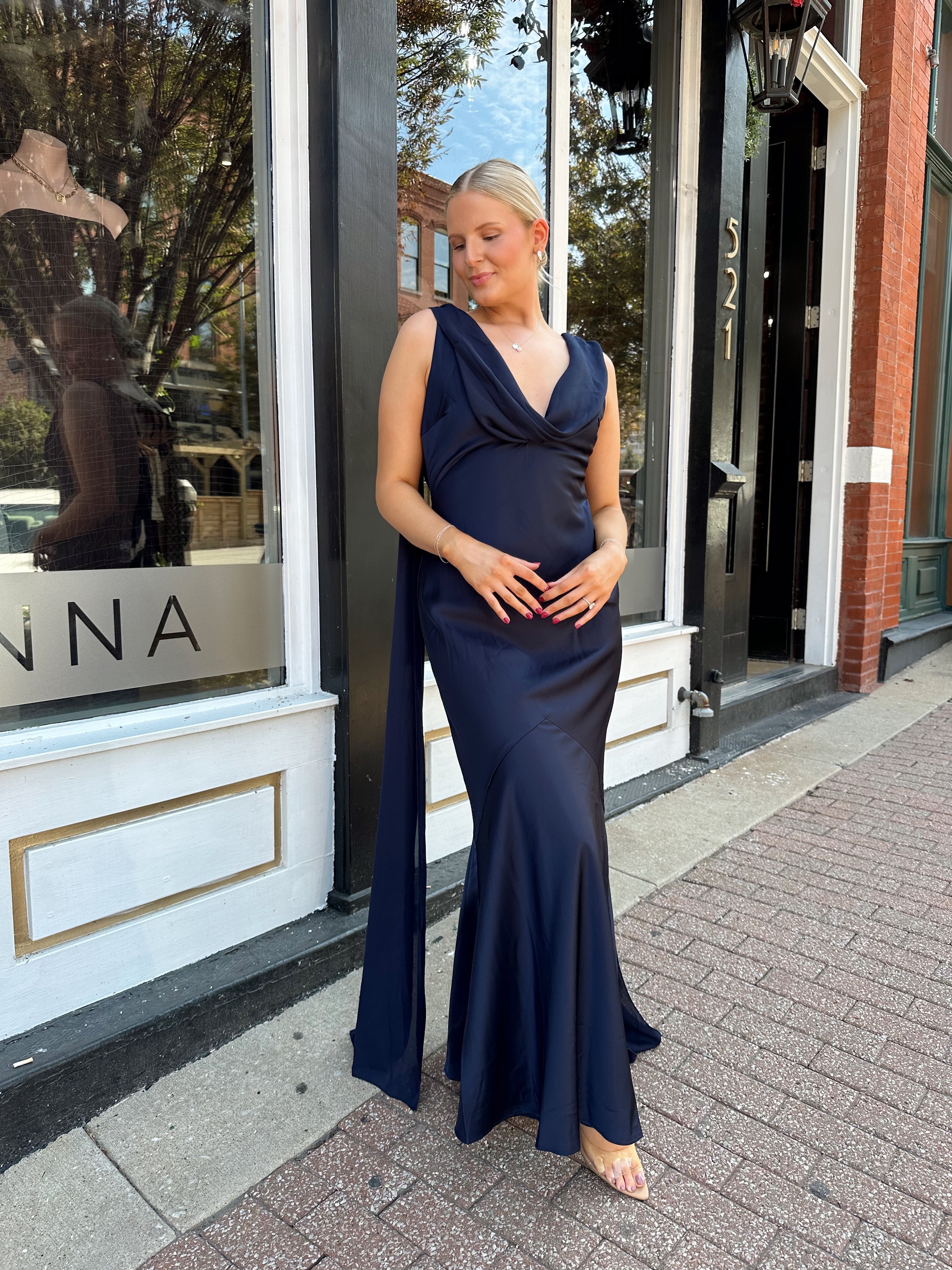 Woman wearing navy blue satin maxi dress with cowl front and back and detachable sash. 