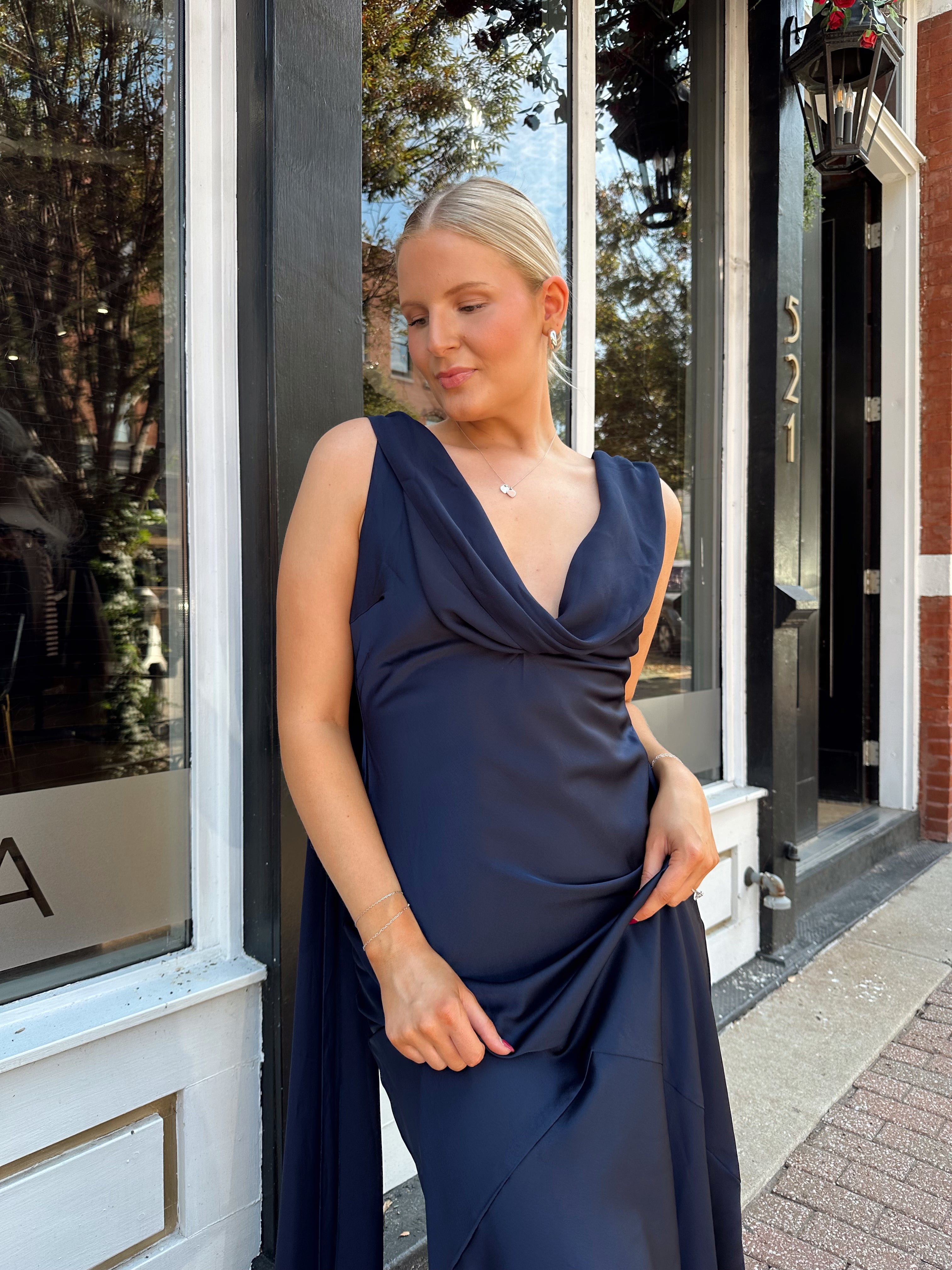 Woman wearing navy blue satin maxi dress with cowl front and back and detachable sash. 