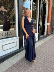 Woman wearing navy blue satin maxi dress with cowl front and back and detachable sash. 