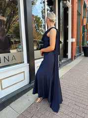 Woman wearing navy blue satin maxi dress with cowl front and back and detachable sash. 