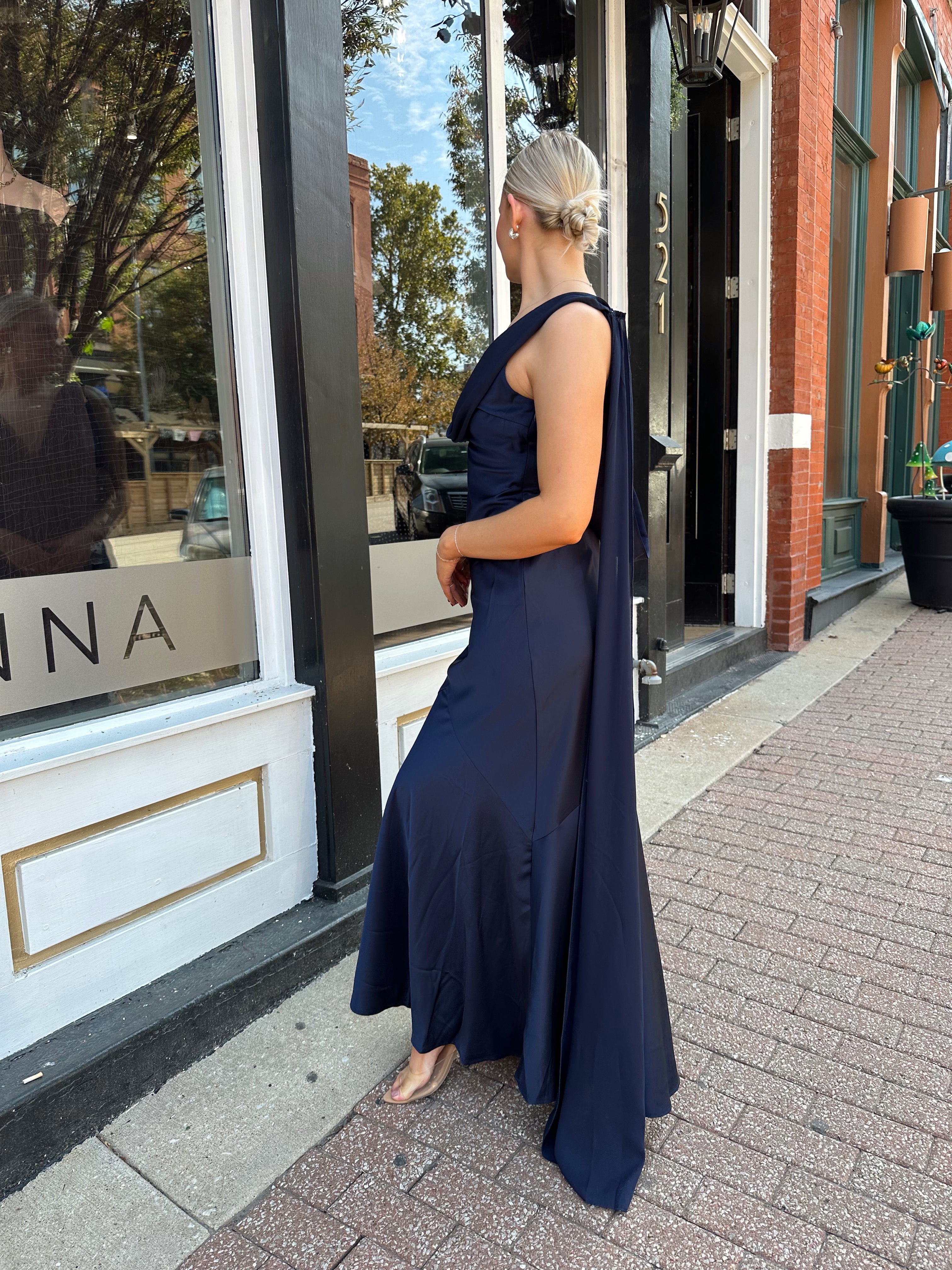 Woman wearing navy blue satin maxi dress with cowl front and back and detachable sash. 