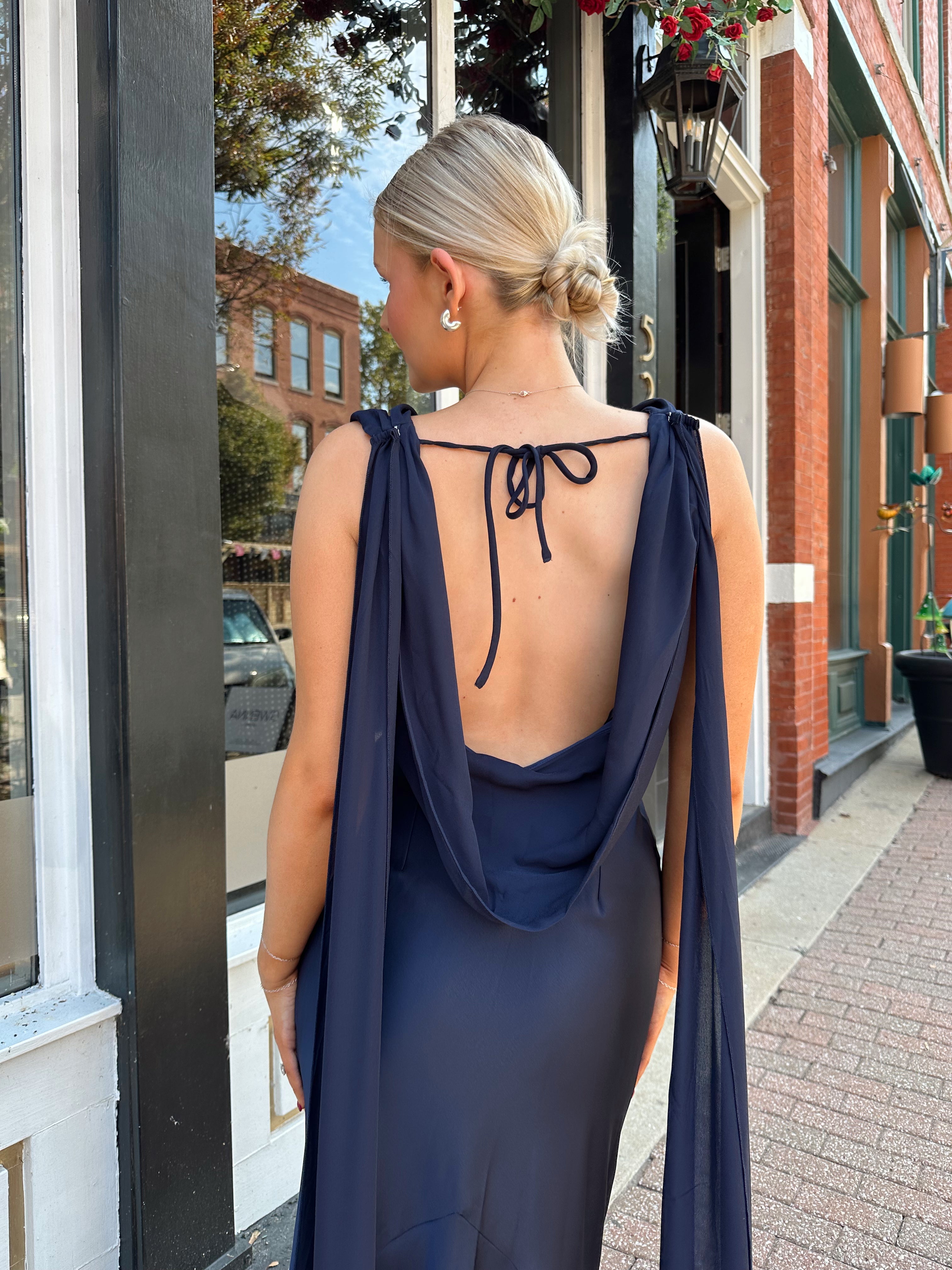 Woman wearing navy blue satin maxi dress with cowl front and back and detachable sash. 