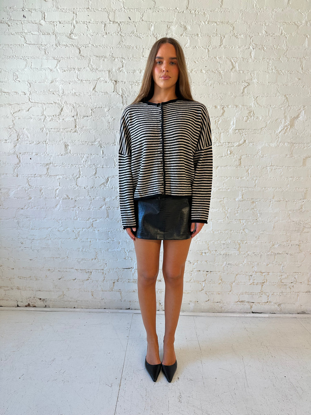 Woman wearing black striped knit cardigan with black high waisted mini skirt. 