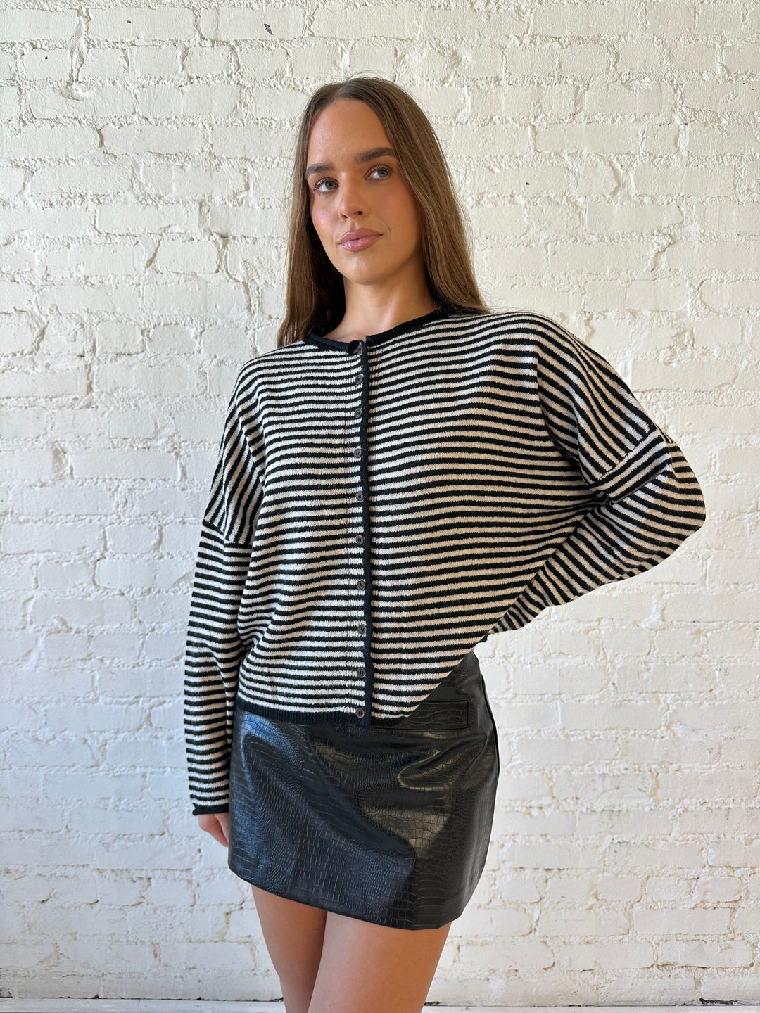 Woman wearing black striped knit cardigan with black high waisted mini skirt. 
