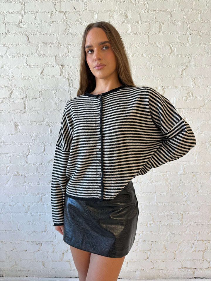 Woman wearing black striped knit cardigan with black high waisted mini skirt. 