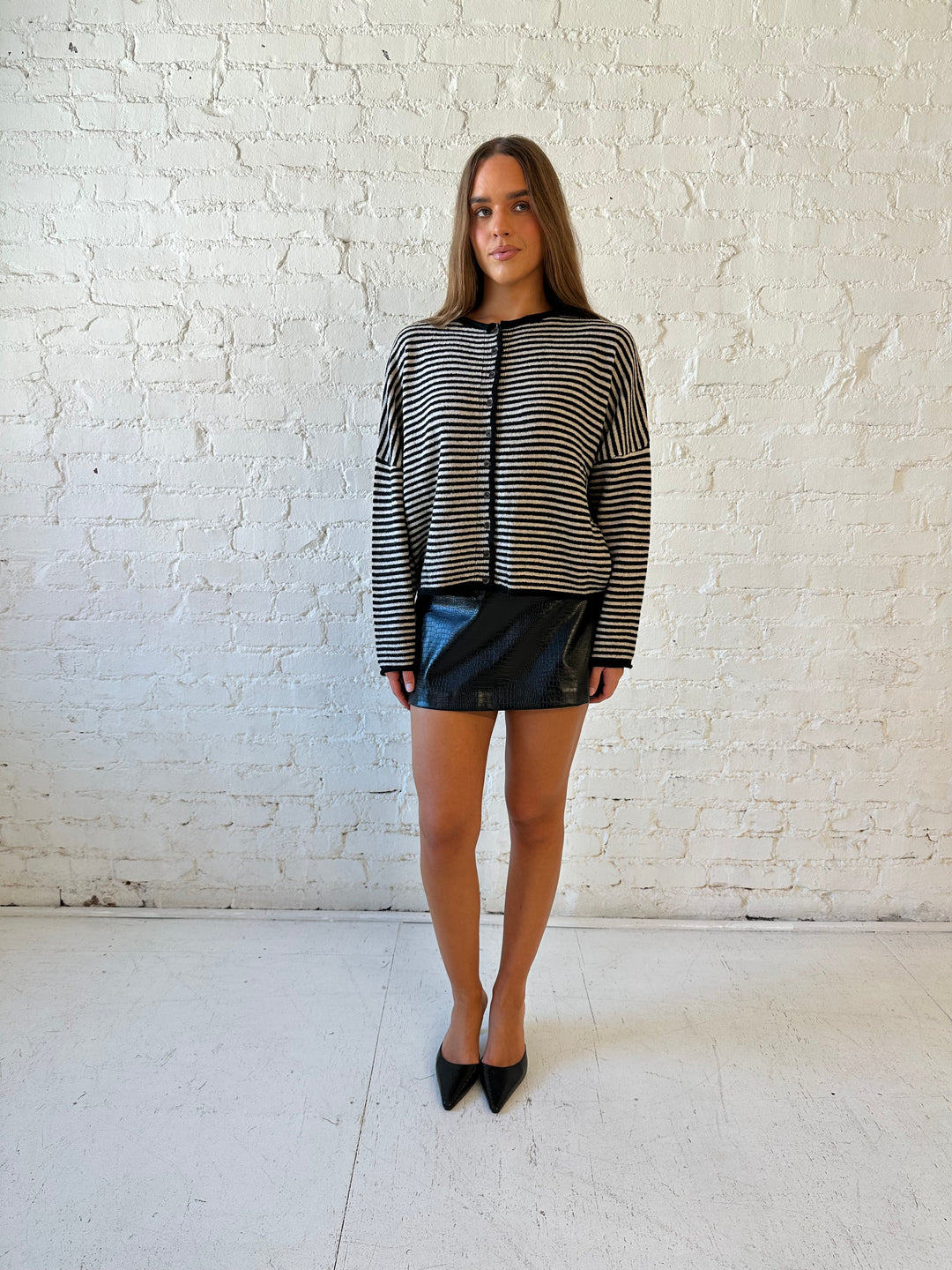 Woman wearing black striped knit cardigan with black high waisted mini skirt. 