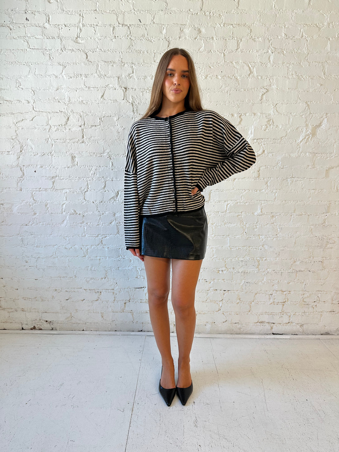 Woman wearing black striped knit cardigan with black high waisted mini skirt. 