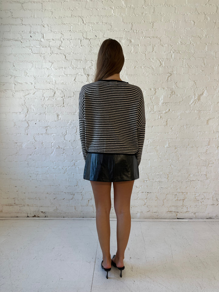 Woman wearing black striped knit cardigan with black high waisted mini skirt. 